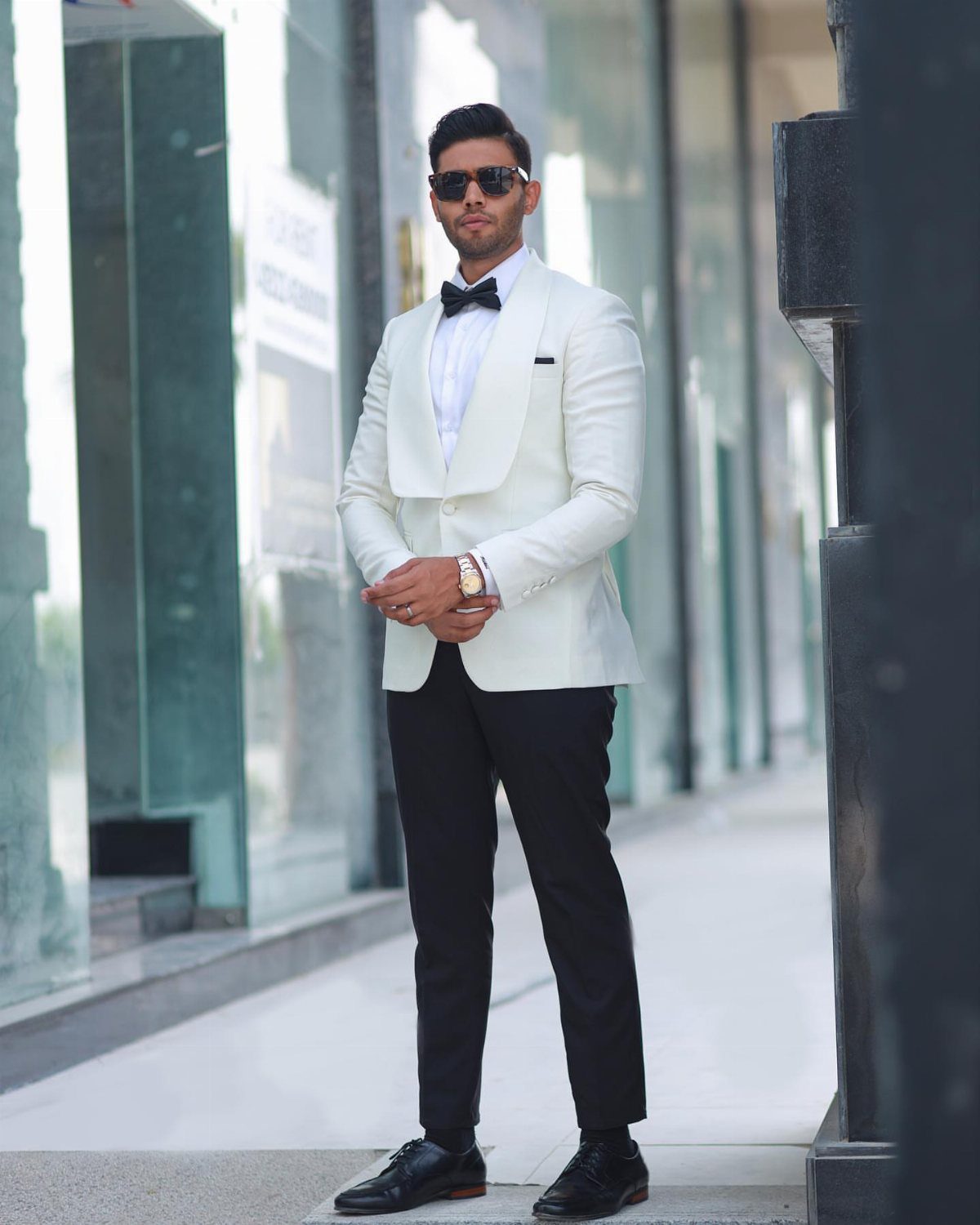 Man in a white dinner jacket, black bow tie, and sunglasses standing on a sidewalk.