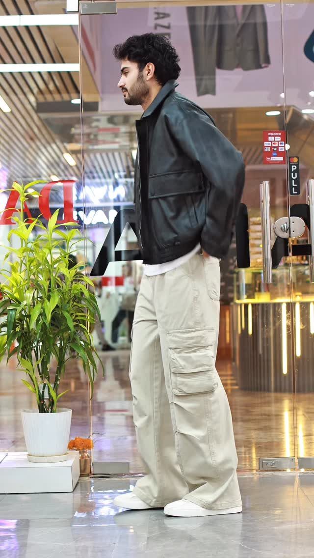 Man standing in profile wearing a black leather jacket and wide-leg khaki cargo pants.