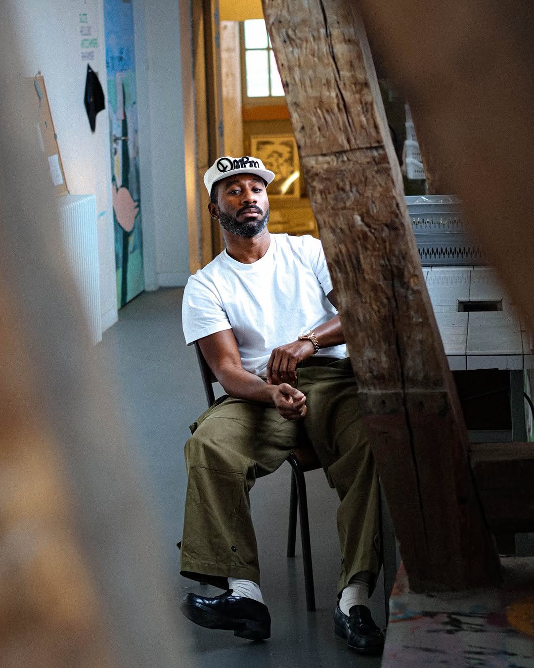 A man sitting in a chair wearing khaki cargo pants, a white t-shirt, and black loafers.