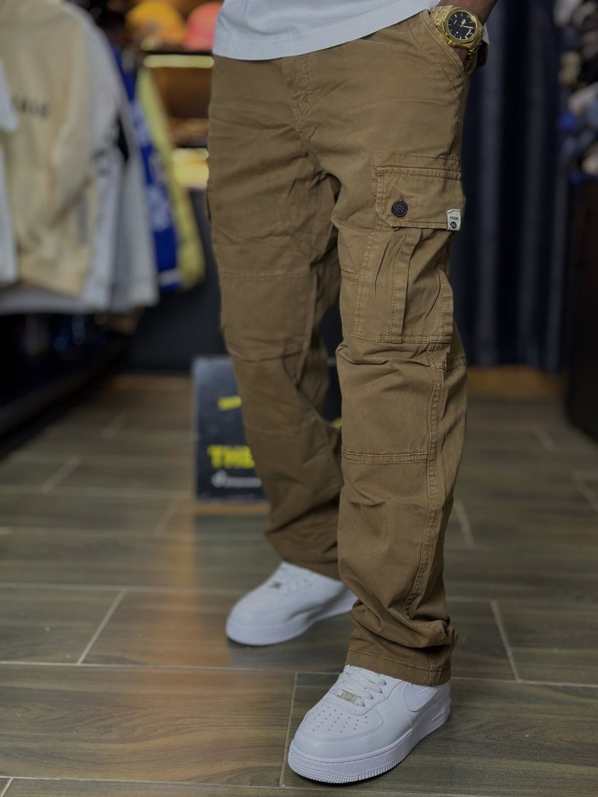 Person wearing khaki cargo pants and white sneakers standing on a wooden floor.