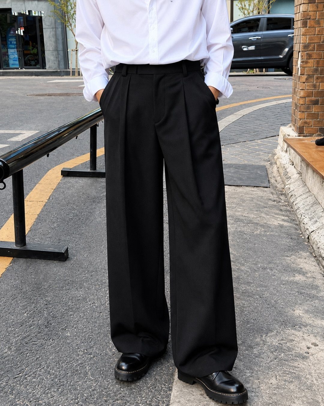 A person wearing a white shirt, wide-leg black trousers, and black leather shoes standing on a street.