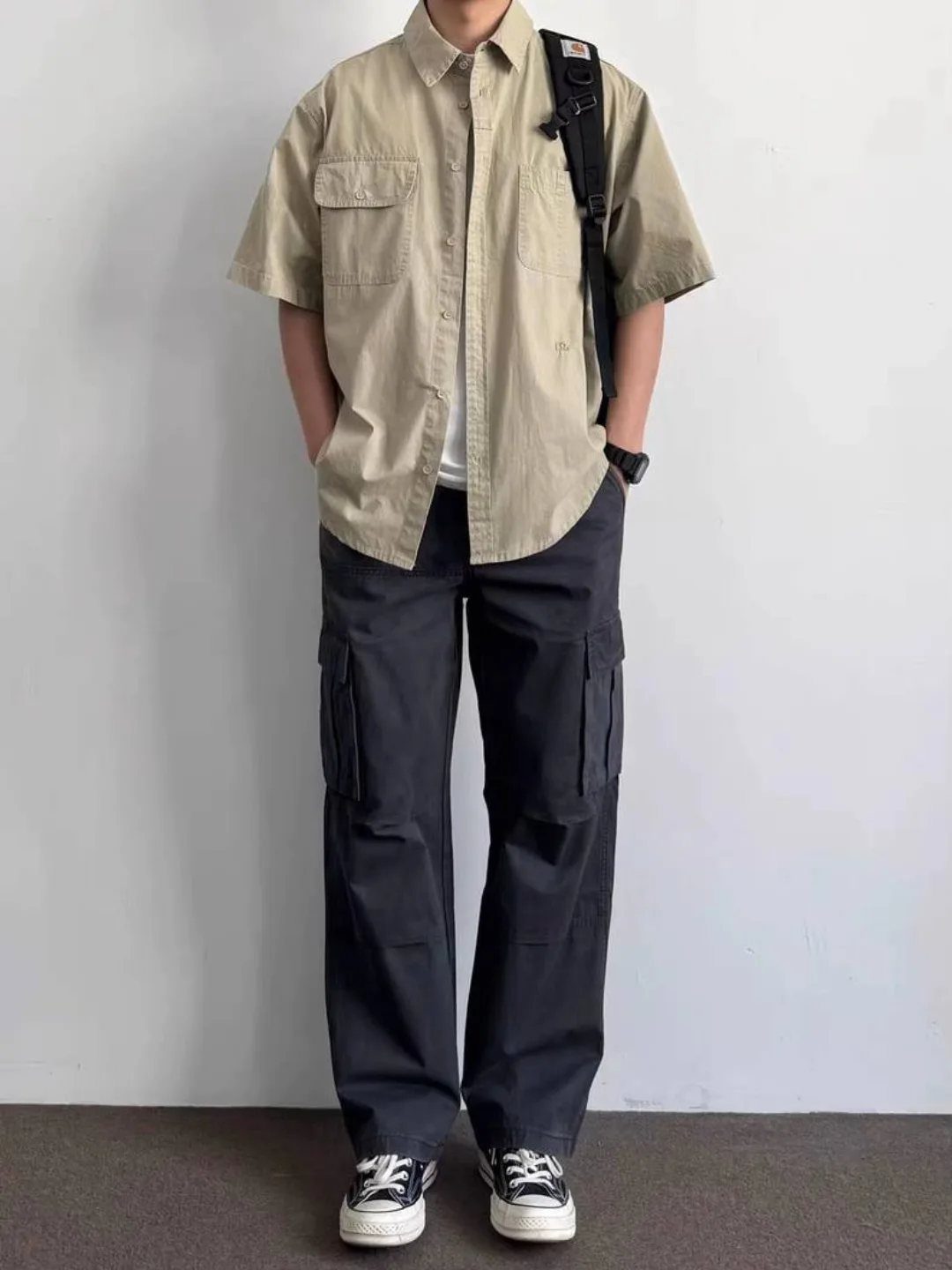 A person wearing a tan short-sleeved shirt and dark grey loose-fit cargo pants.