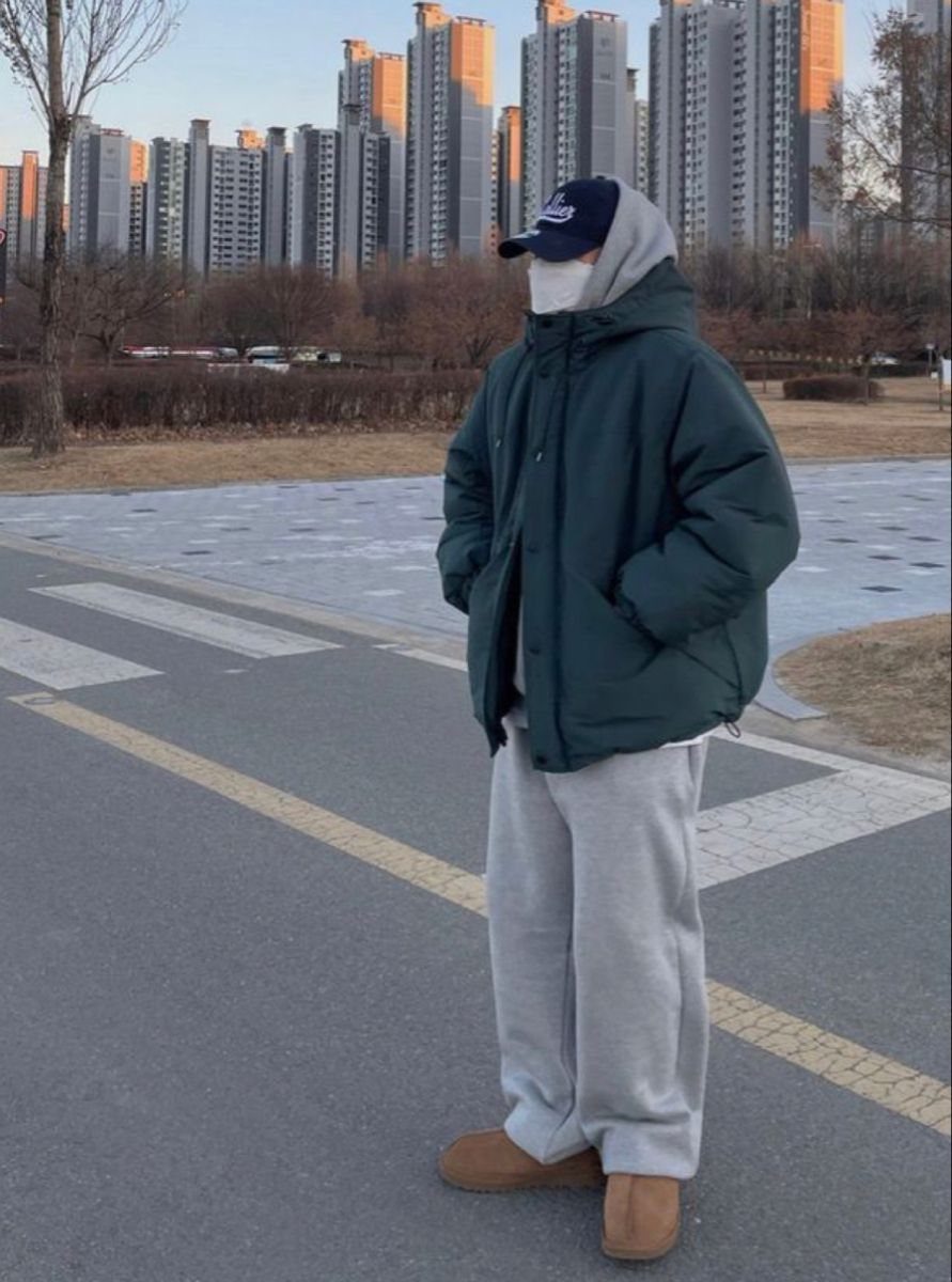A person wearing a green puffer jacket, grey sweatpants, and tan sheepskin boots standing outdoors.