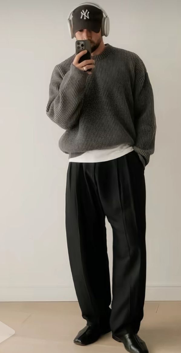 Man in a grey ribbed sweater and black wide-leg trousers posing for a mirror selfie.