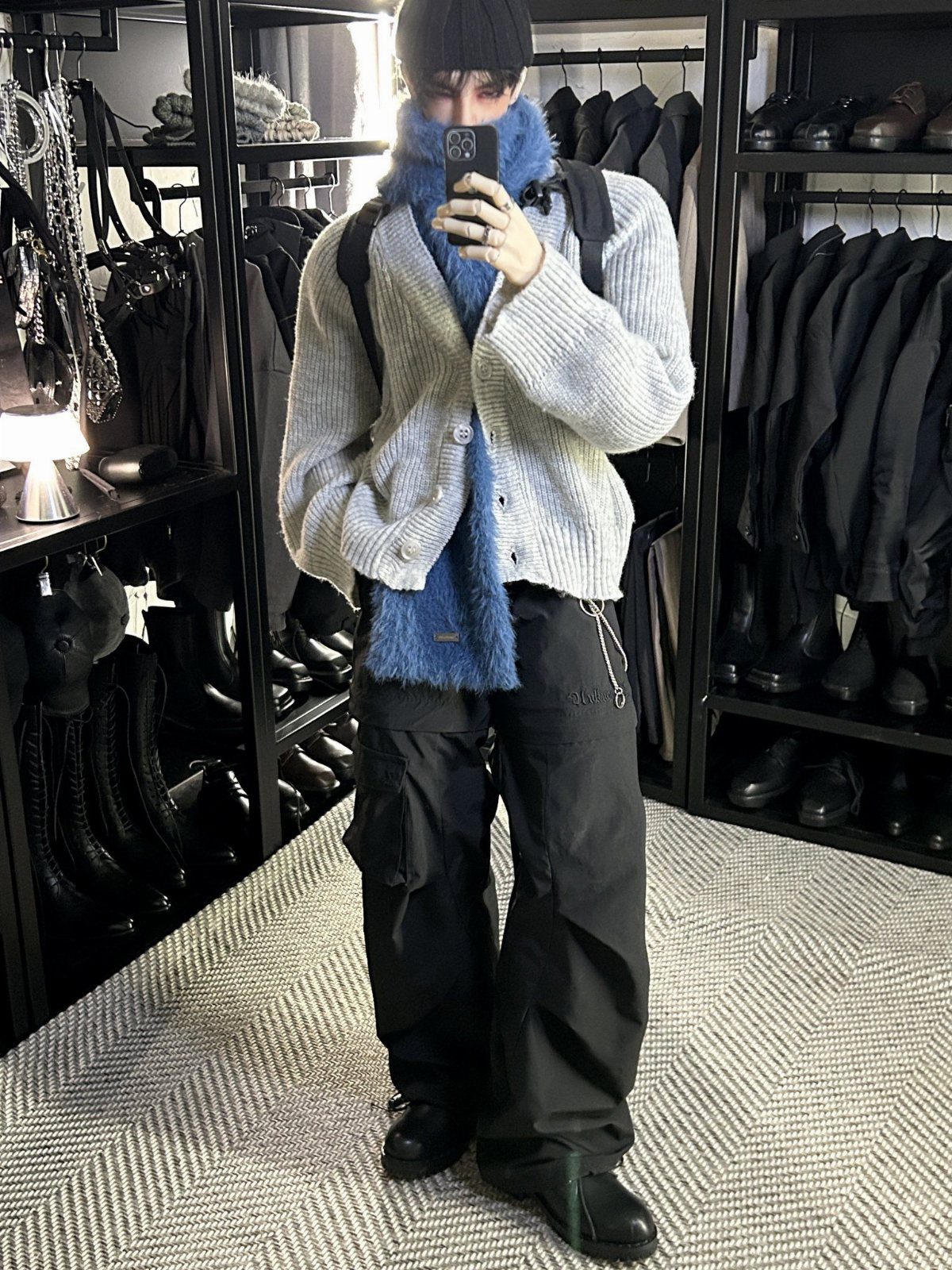 A person in a grey cardigan and black cargo pants taking a mirror selfie.