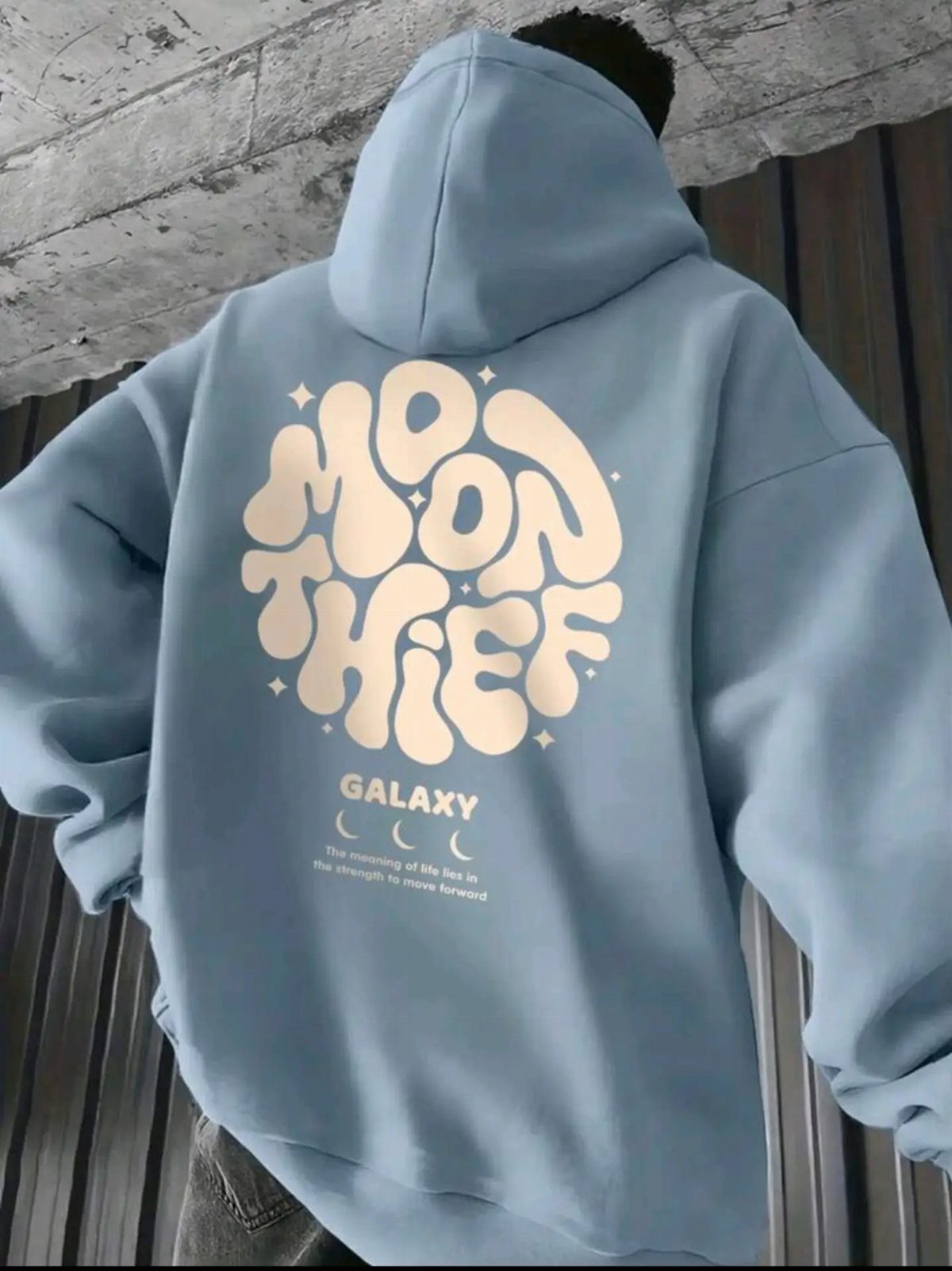 Back view of a person wearing a light blue oversized hoodie with a cream graphic design.