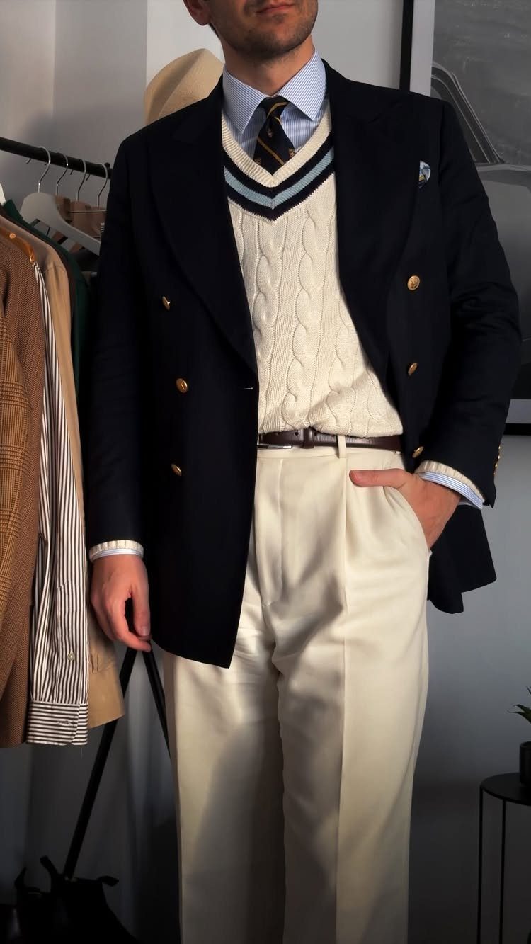Man wearing a navy blazer, cream sweater, and cream trousers with a brown leather belt.