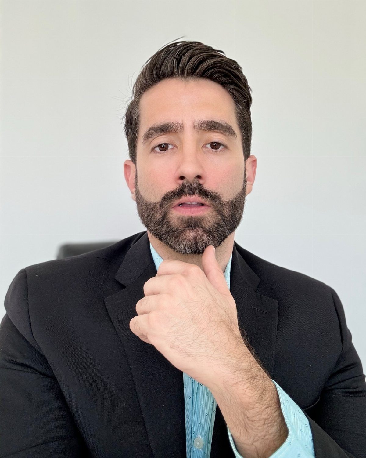 A man with neatly styled dark hair and a well-groomed beard wearing a black suit jacket.
