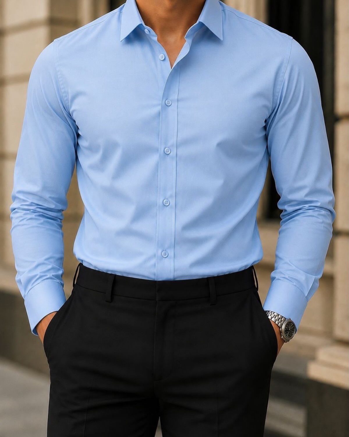 A man wearing a light blue button-down dress shirt and black trousers.