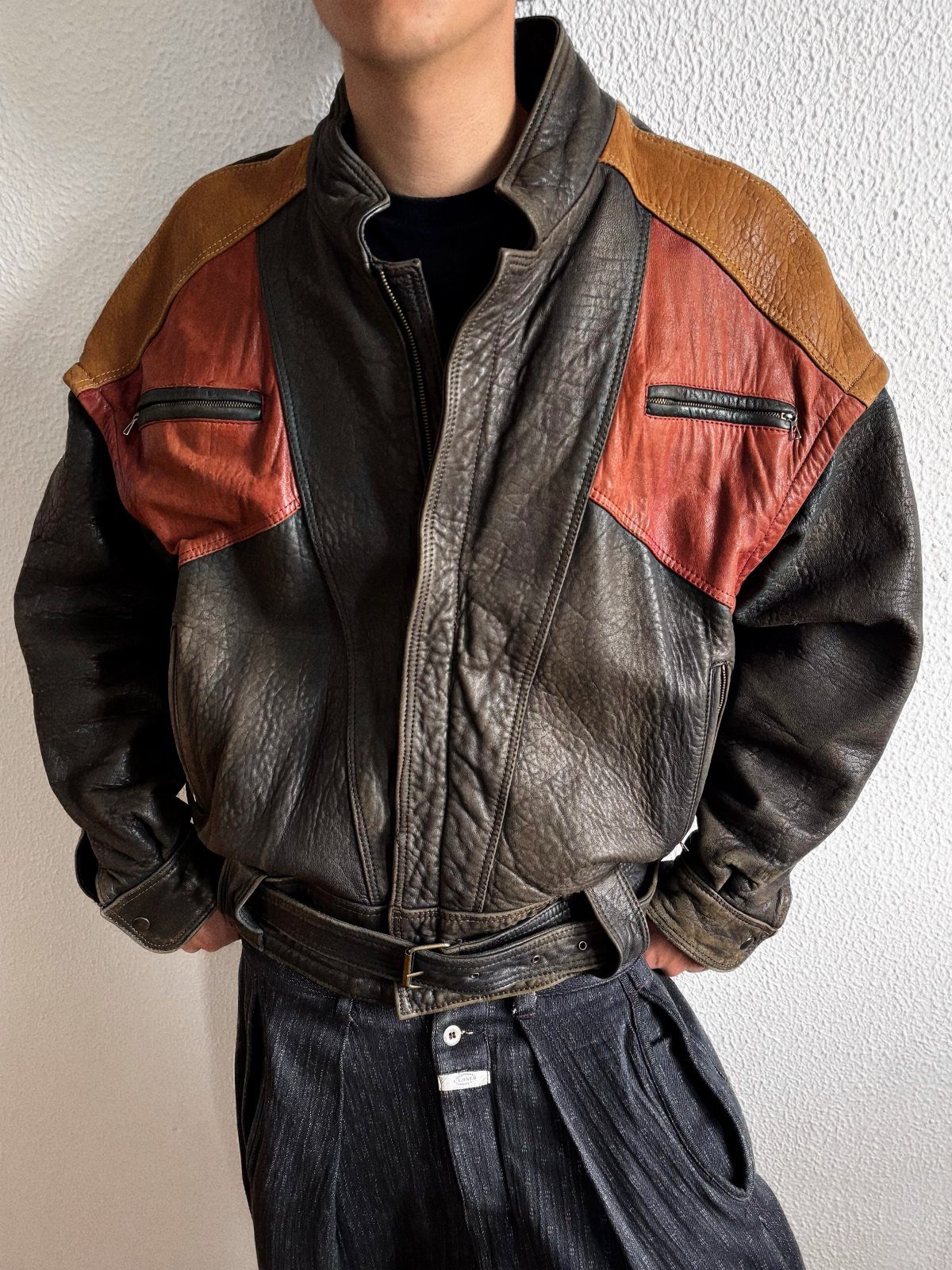 A person wearing a vintage color-blocked leather jacket with brown and red panels and dark trousers.