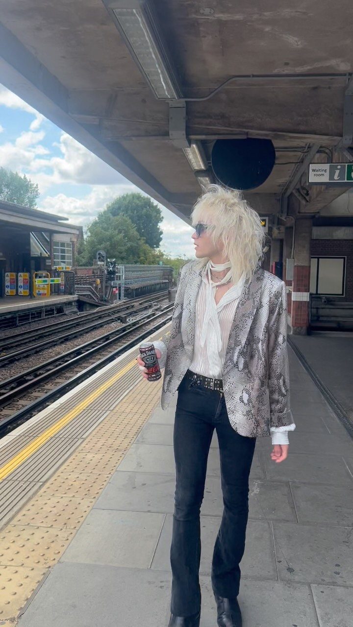 Person in snakeskin blazer and flared trousers standing on a train platform.