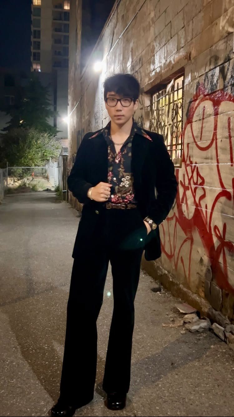 Man posing in an alley wearing a black velvet suit and a floral patterned shirt.