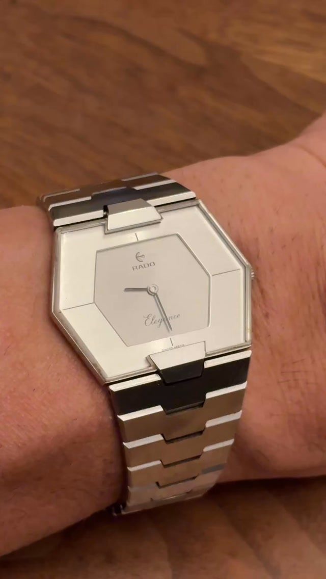 A silver octagonal metal watch with a link bracelet worn on a person's wrist.