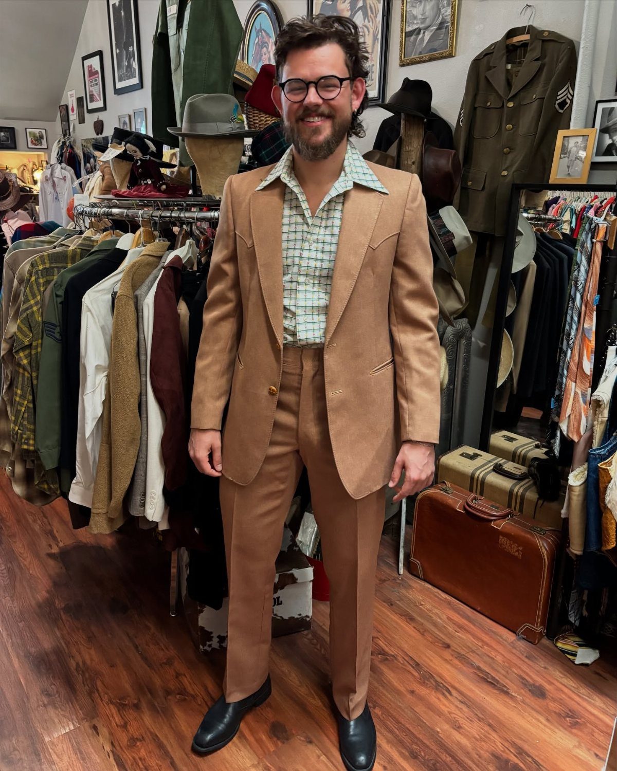 Man wearing a tan vintage suit with wide lapels and a checkered shirt in a clothing store.