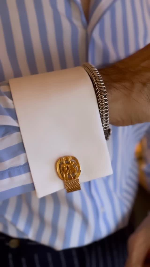 A man's arm wearing a blue striped shirt with a white French cuff and gold cufflink.