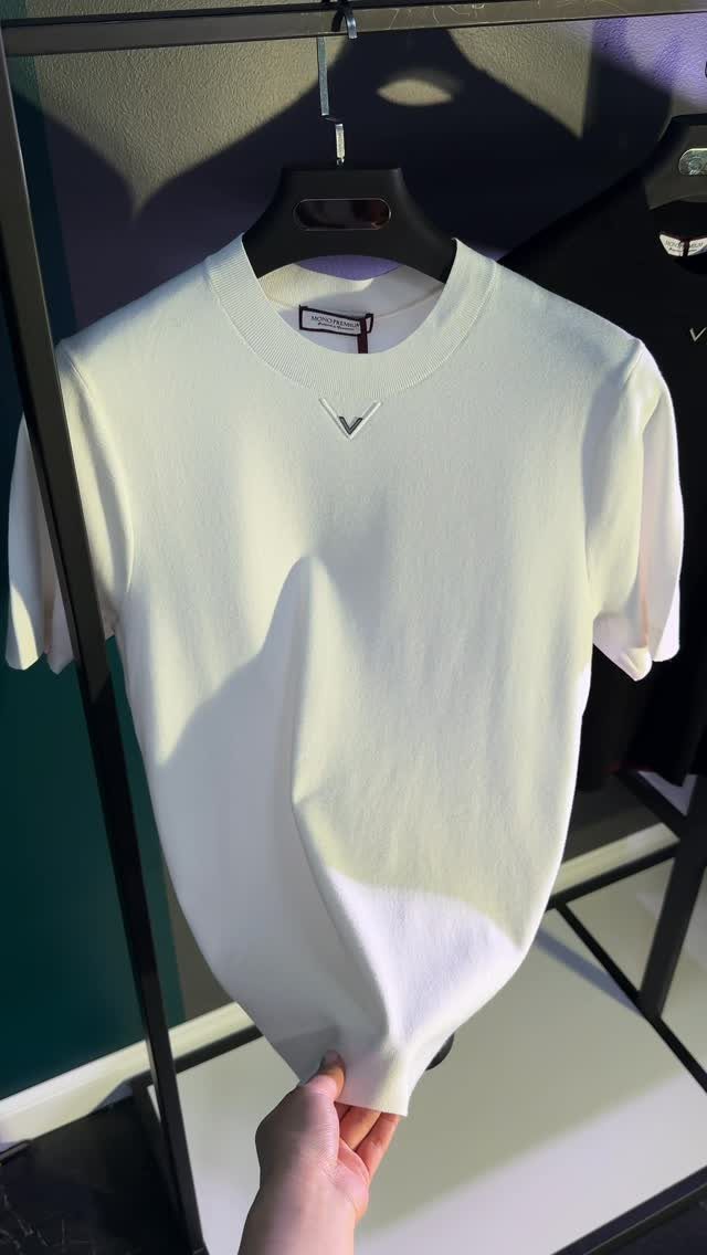 A white short-sleeved knit shirt hanging on a black hanger on a clothing rack.