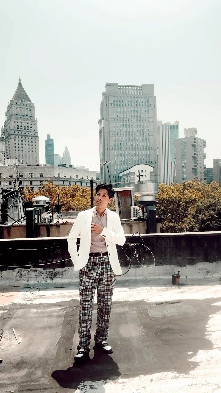 Man in a white blazer and plaid trousers posing on a city rooftop.
