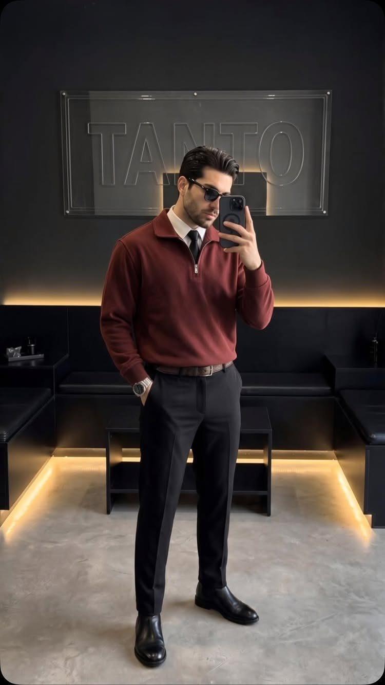 Man in maroon pullover, white shirt, tie, and black trousers posing for a mirror selfie.