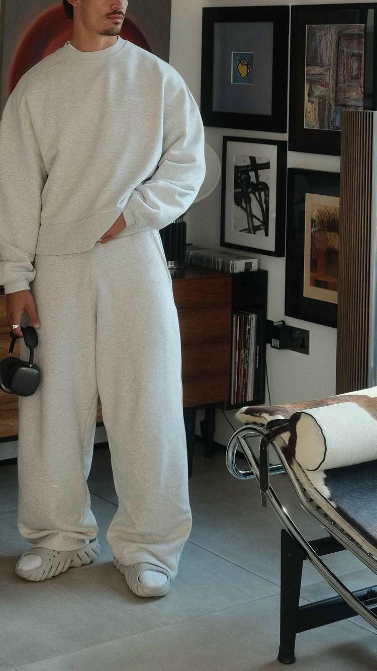 Man wearing a matching light grey sweatshirt and wide-leg lounge pants in a modern room.
