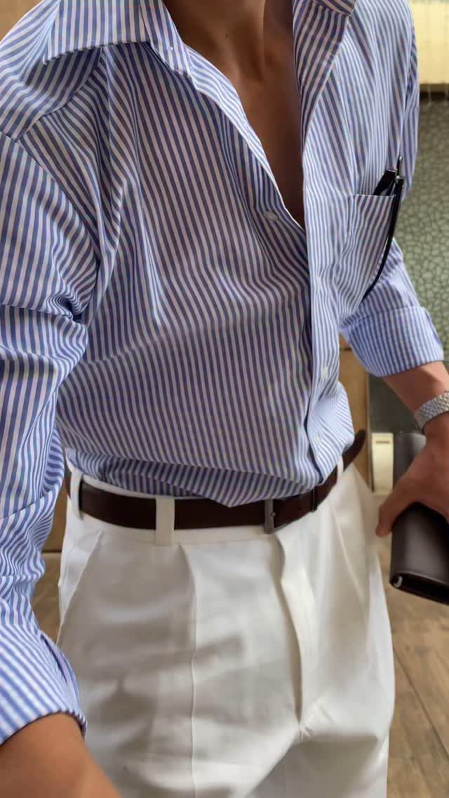 Man wearing a blue striped shirt and white trousers with a brown leather belt.