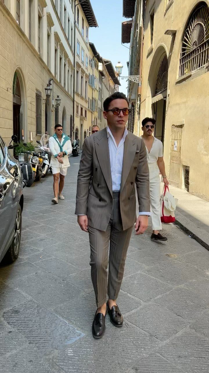 Man walking through an Italian street wearing a stylish brown double-breasted suit and white shirt.