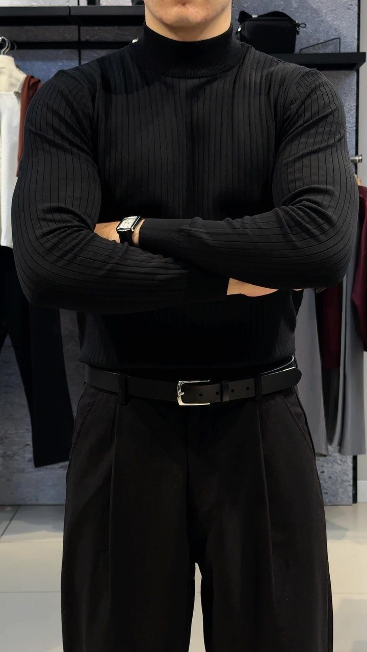 Man wearing a black ribbed turtleneck, black trousers, and a black leather belt.
