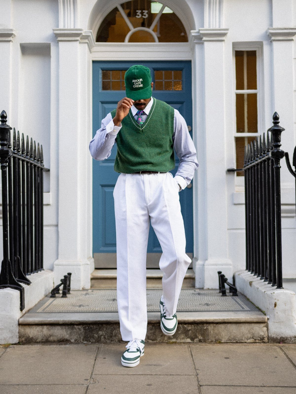 Man wearing a green sweater vest, white trousers, and a green cap walking down steps.
