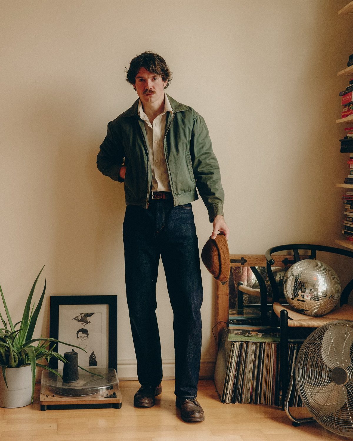 A man in a retro-inspired outfit stands in a room with vinyl records and a disco ball.