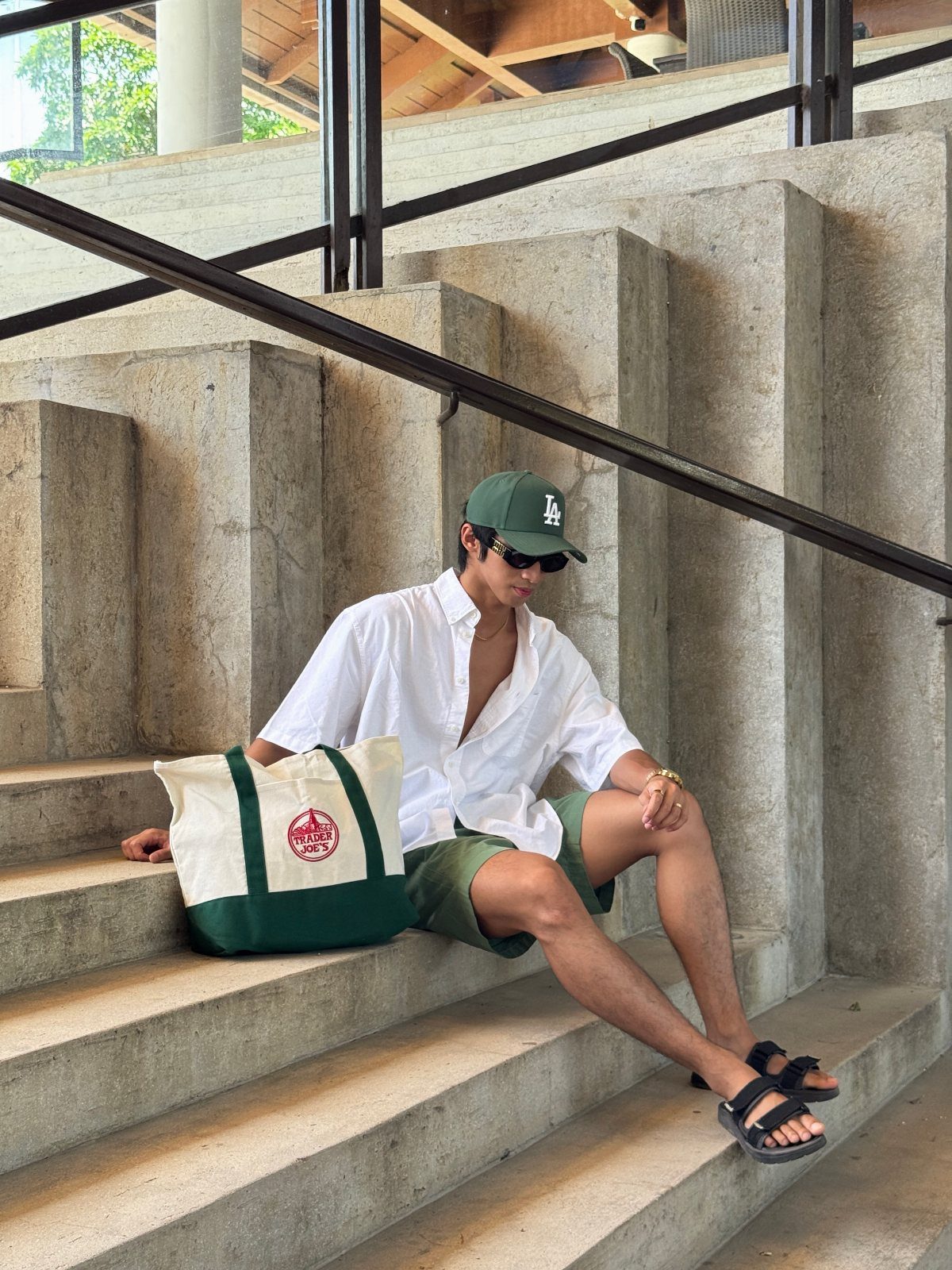 A man sitting on concrete stairs next to a large cream and green canvas beach bag.