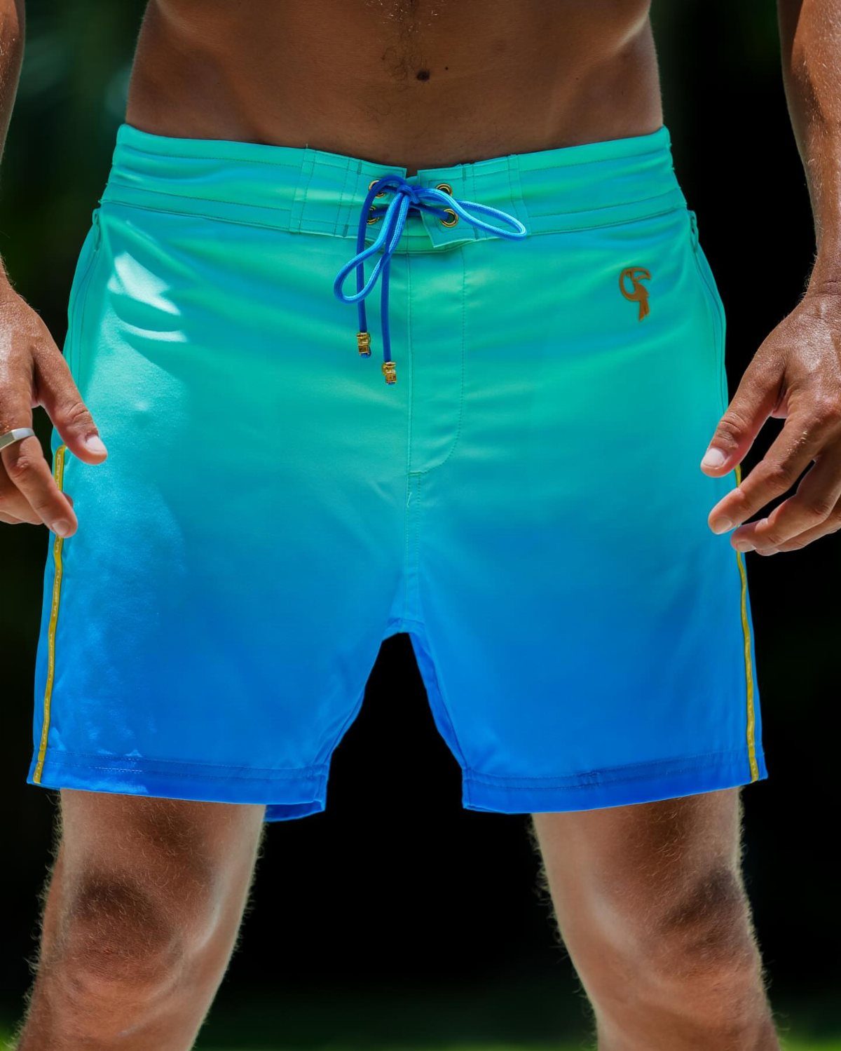Man wearing bright blue and turquoise gradient swim shorts with a drawstring waist.
