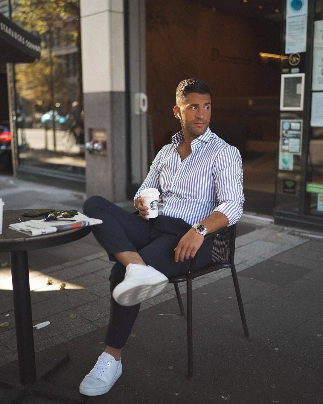 Man in a striped button-down shirt sitting at an outdoor cafe table with coffee.
