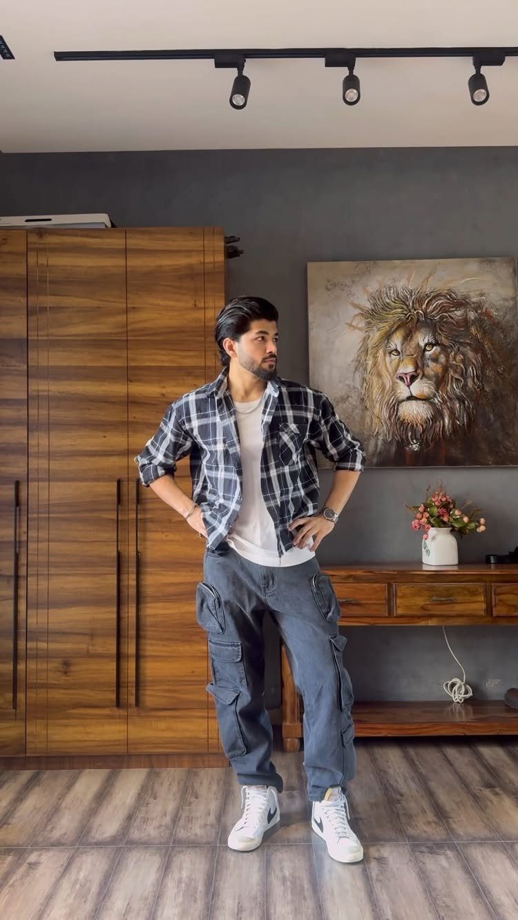 Man posing in a plaid shirt, white t-shirt, grey cargo pants, and white sneakers.