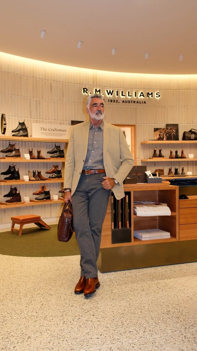 Man in a beige blazer, blue shirt, and grey trousers walking through a clothing store.