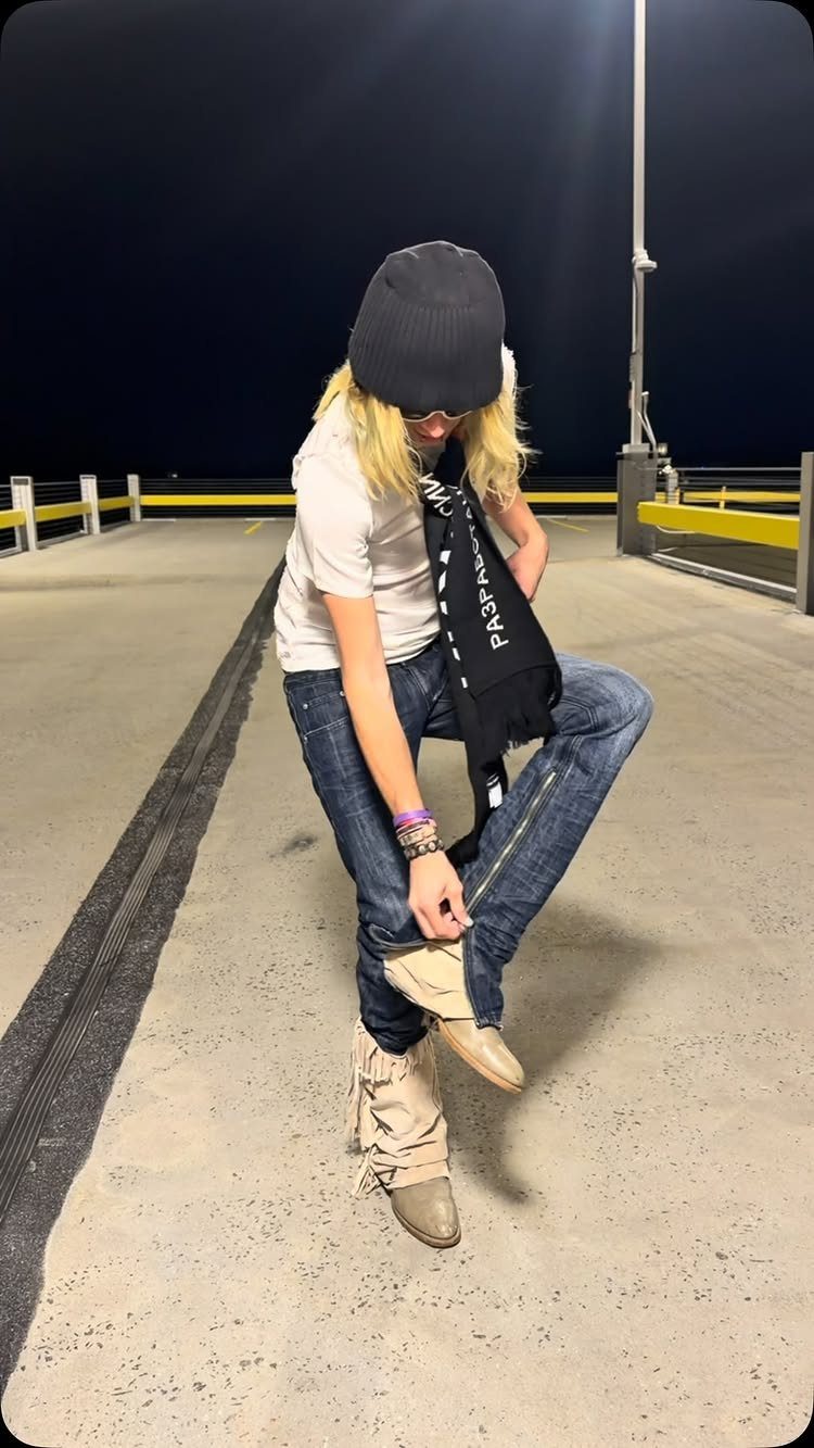 A person wearing tan fringed moccasin boots and blue jeans standing on concrete at night.