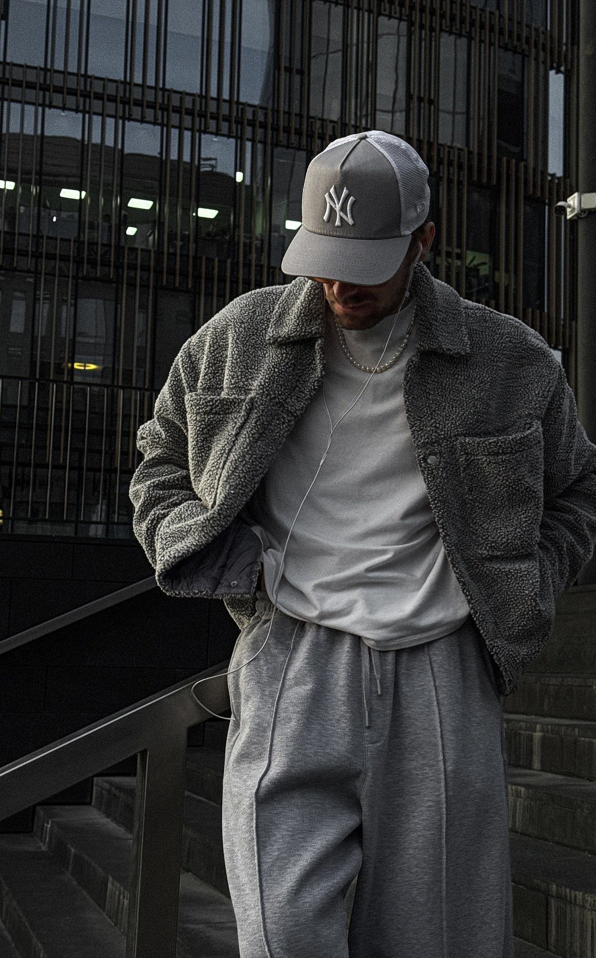 A man dressed in grey streetwear including a fleece jacket, baseball cap, and sweatpants.