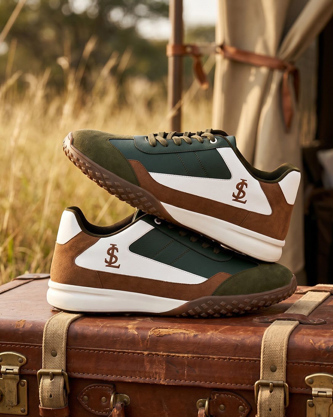 Green and tan sneakers resting on a vintage leather suitcase in a grassy field.