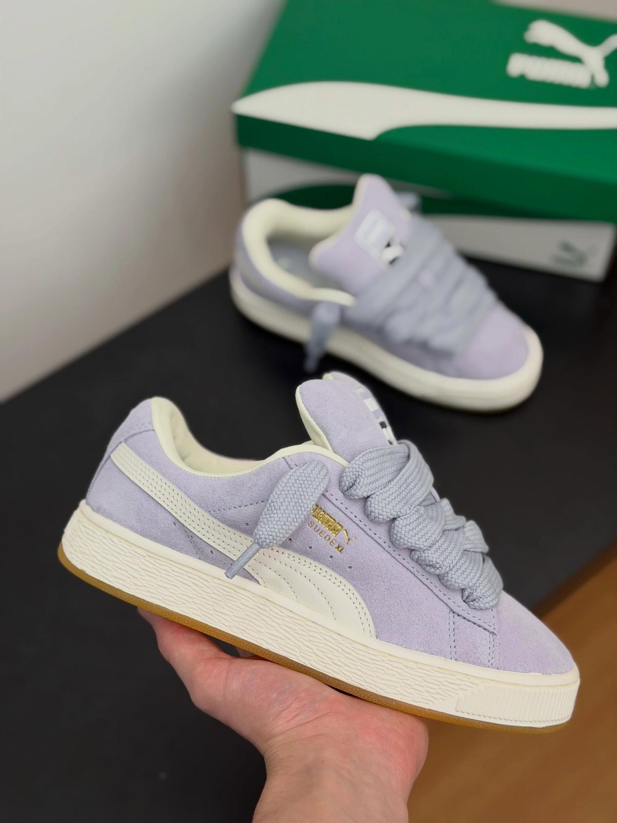 A hand holding a light purple suede Puma sneaker against a blurred background.