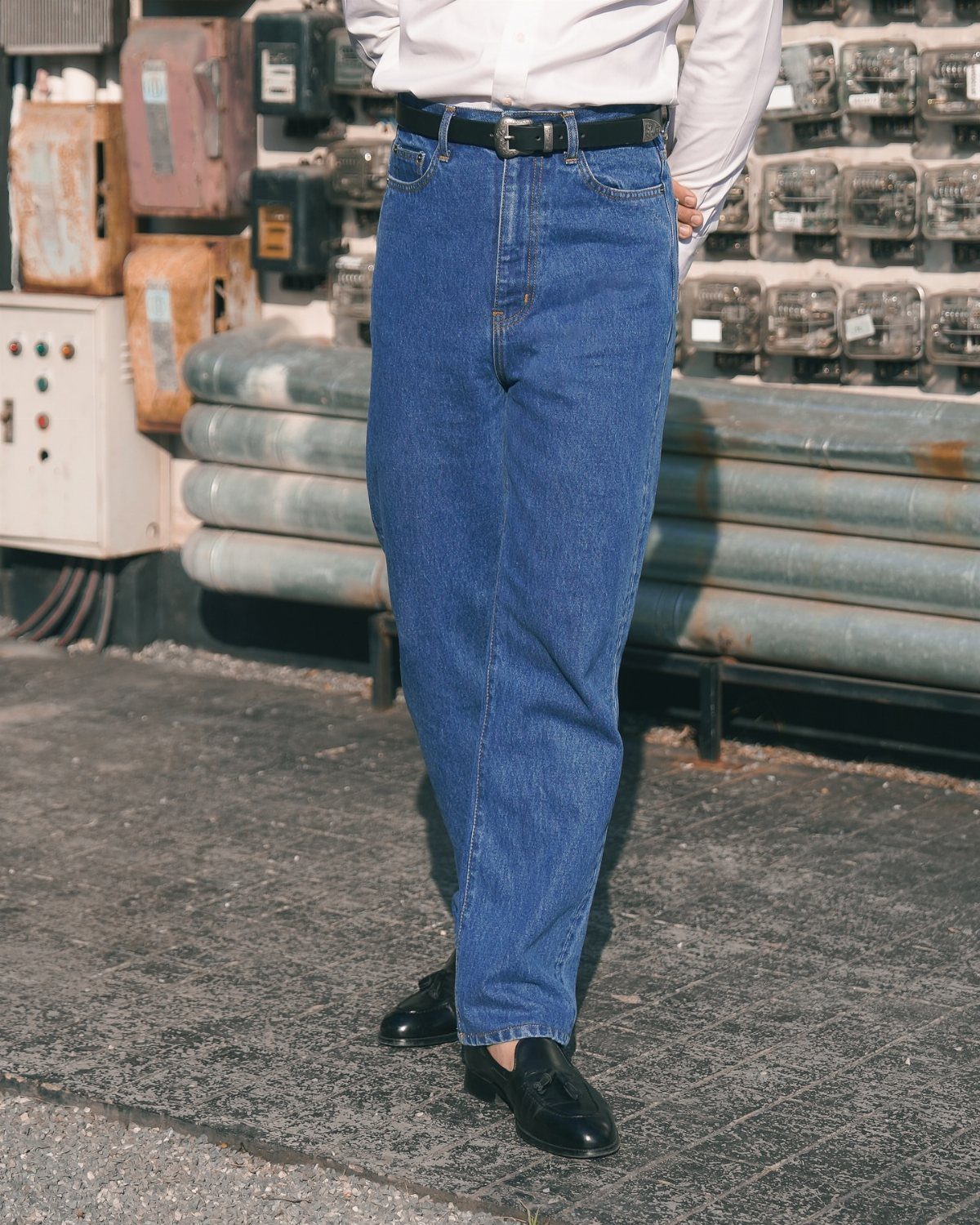A person wearing high-rise blue denim jeans with a black belt and black shoes.
