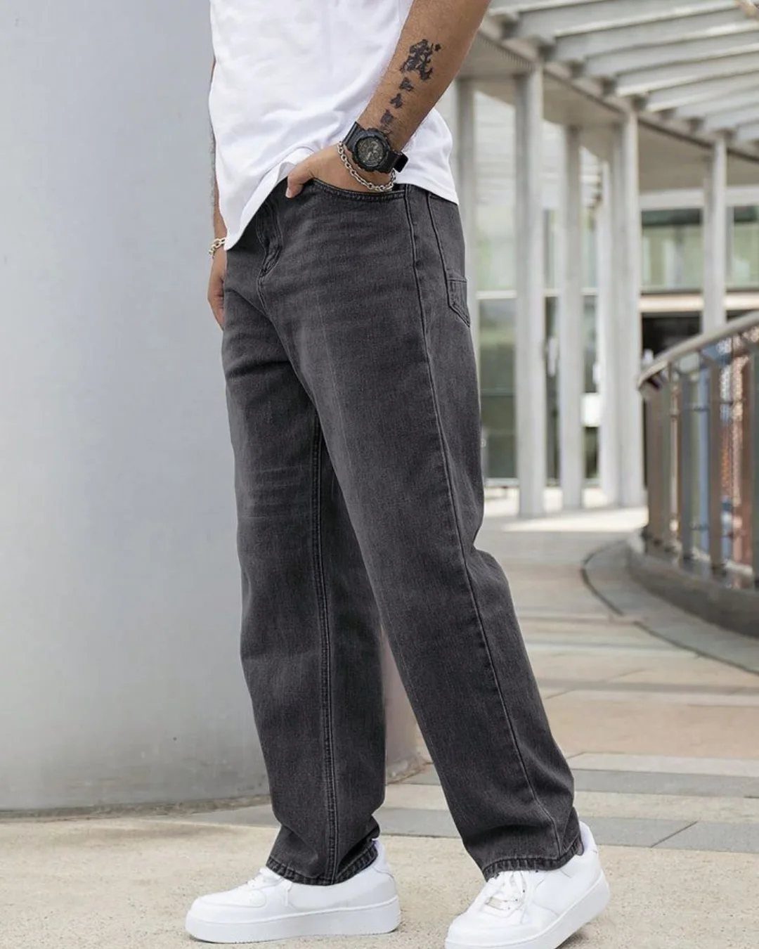 Man wearing dark grey loose-fit denim jeans and white sneakers standing outdoors.