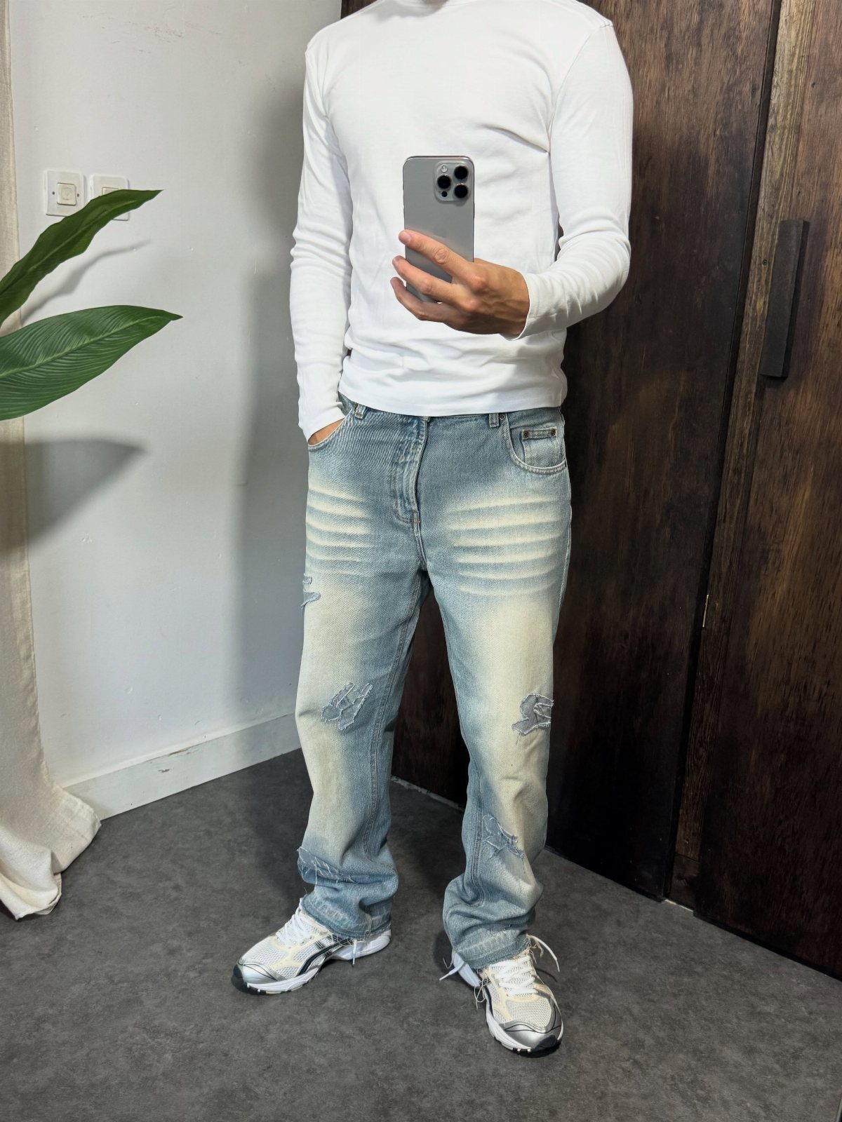 Man wearing light blue ripped denim jeans and a white long-sleeved shirt standing indoors.