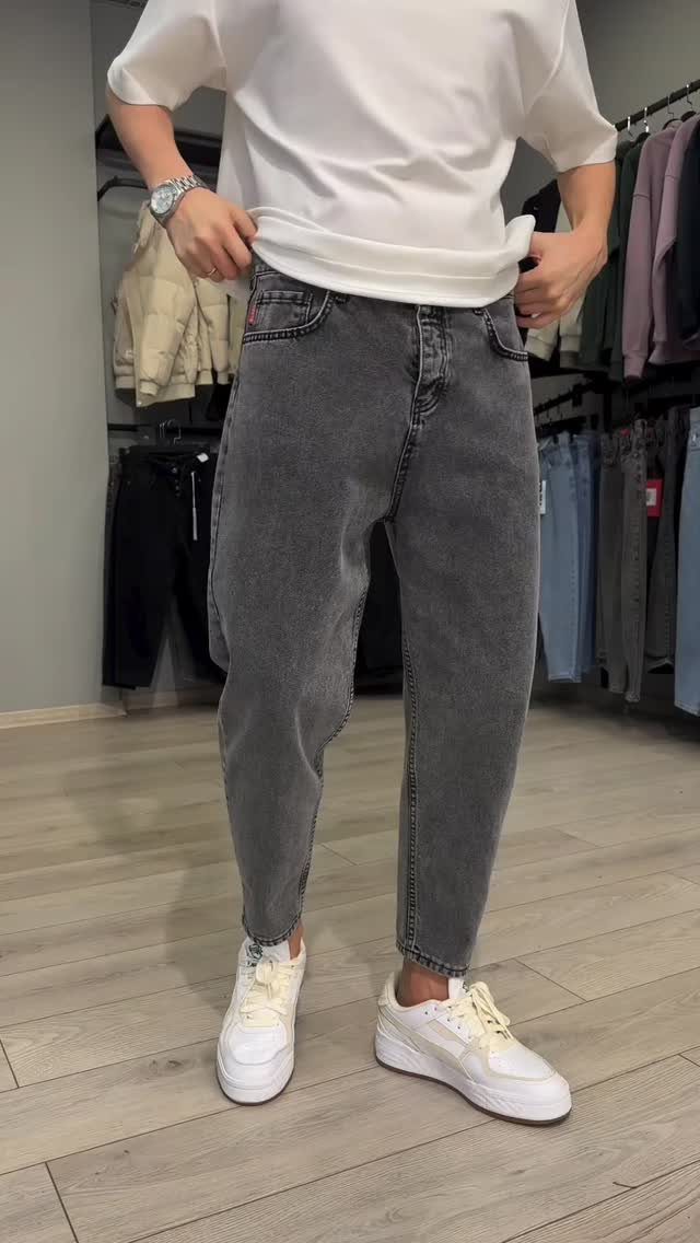 A person wearing grey tapered denim jeans and white sneakers in a clothing store.