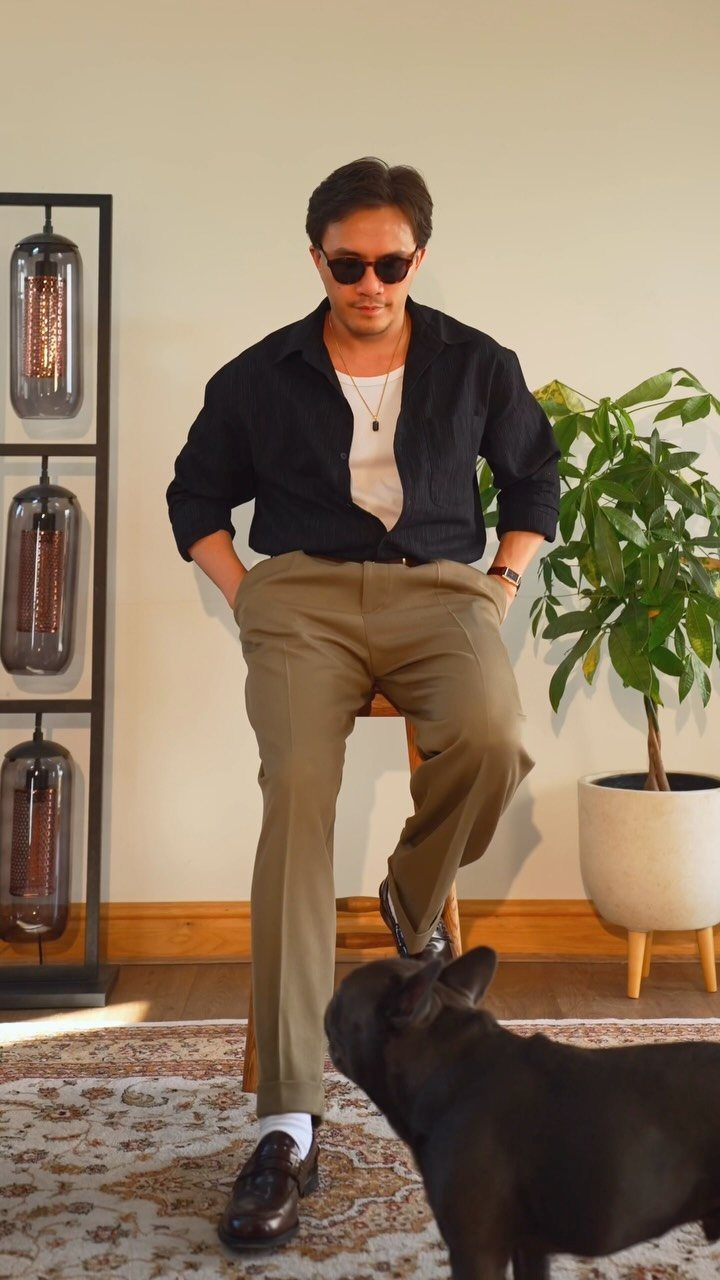Man in retro black shirt, khaki pants, and sunglasses sitting near a dog.