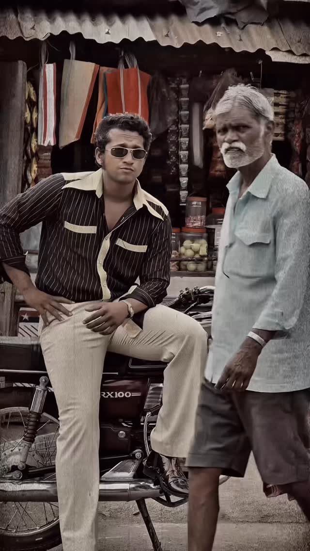 Man in retro striped shirt and sunglasses sitting on a motorcycle in a market.