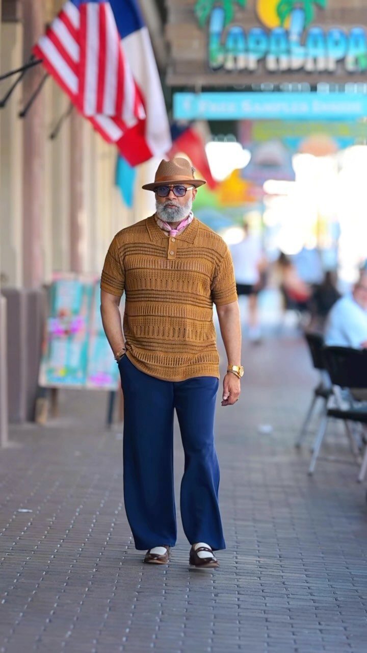 Man in retro brown polo and wide-leg blue trousers walking on a sunny street.