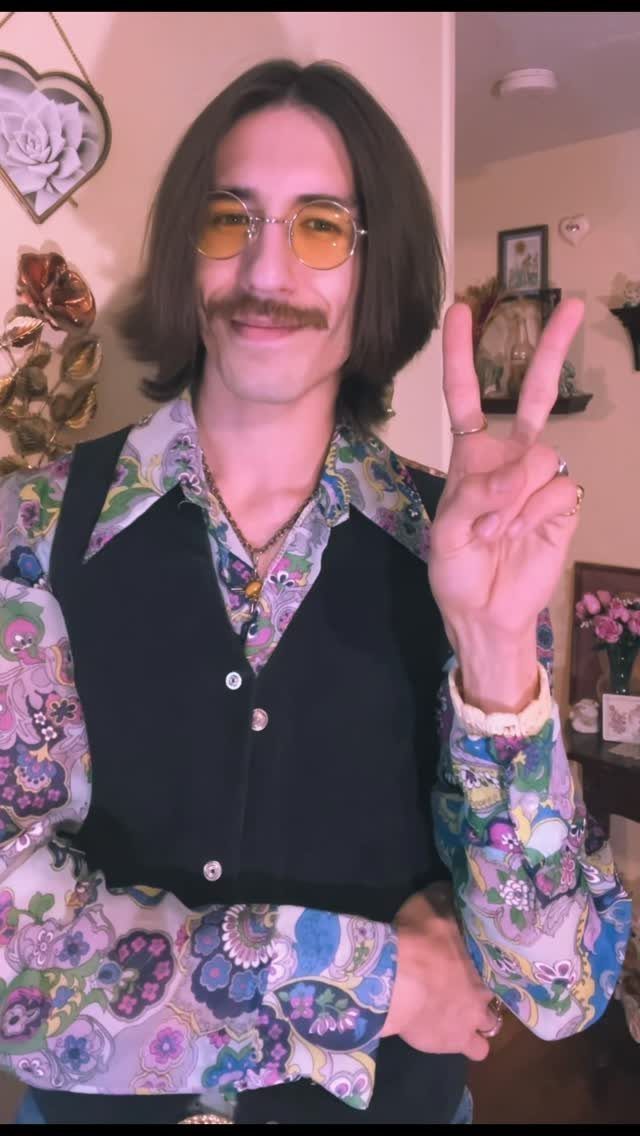 Man with mustache and yellow glasses wearing a colorful floral vintage shirt and waistcoat.