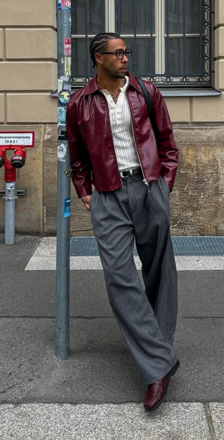 A man wearing a burgundy leather jacket, white shirt, and grey pinstriped trousers standing outdoors.