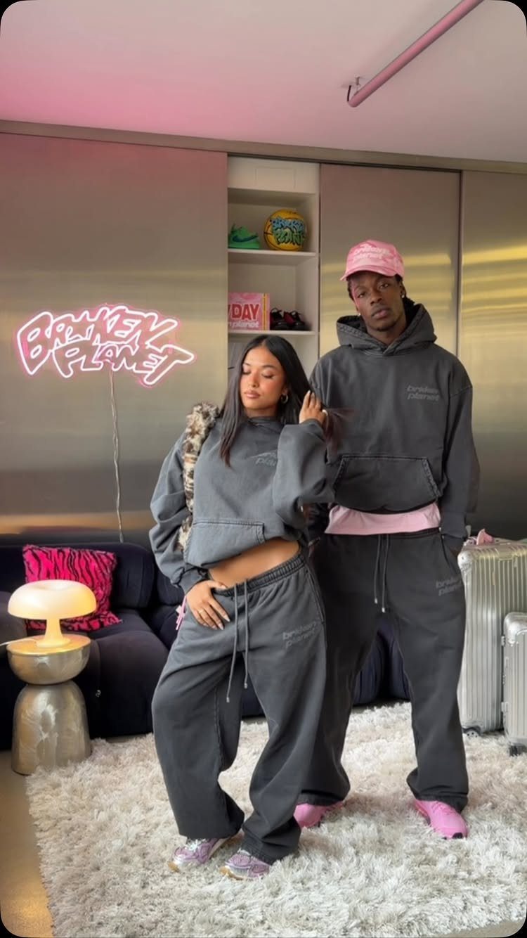 A man and woman posing in matching dark grey hooded sweatshirts and sweatpants.