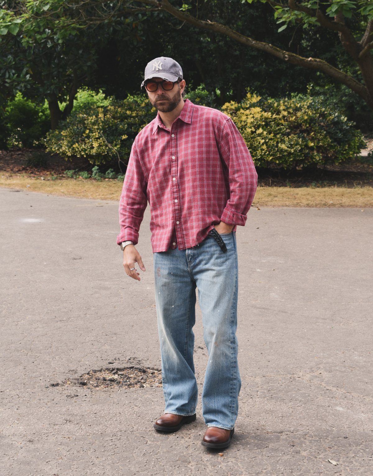 Man wearing a red plaid shirt, blue jeans, brown boots, and a grey baseball cap.