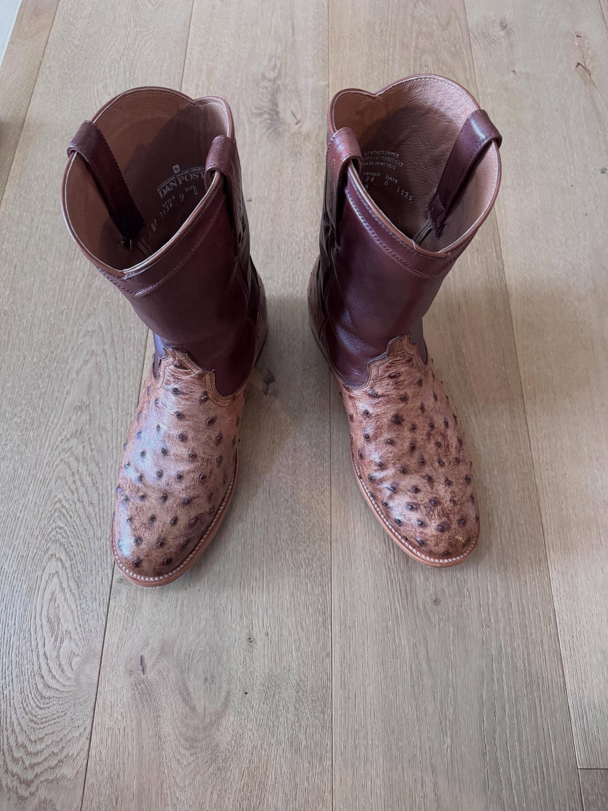 Brown ostrich leather cowboy boots resting on a light wooden floor.