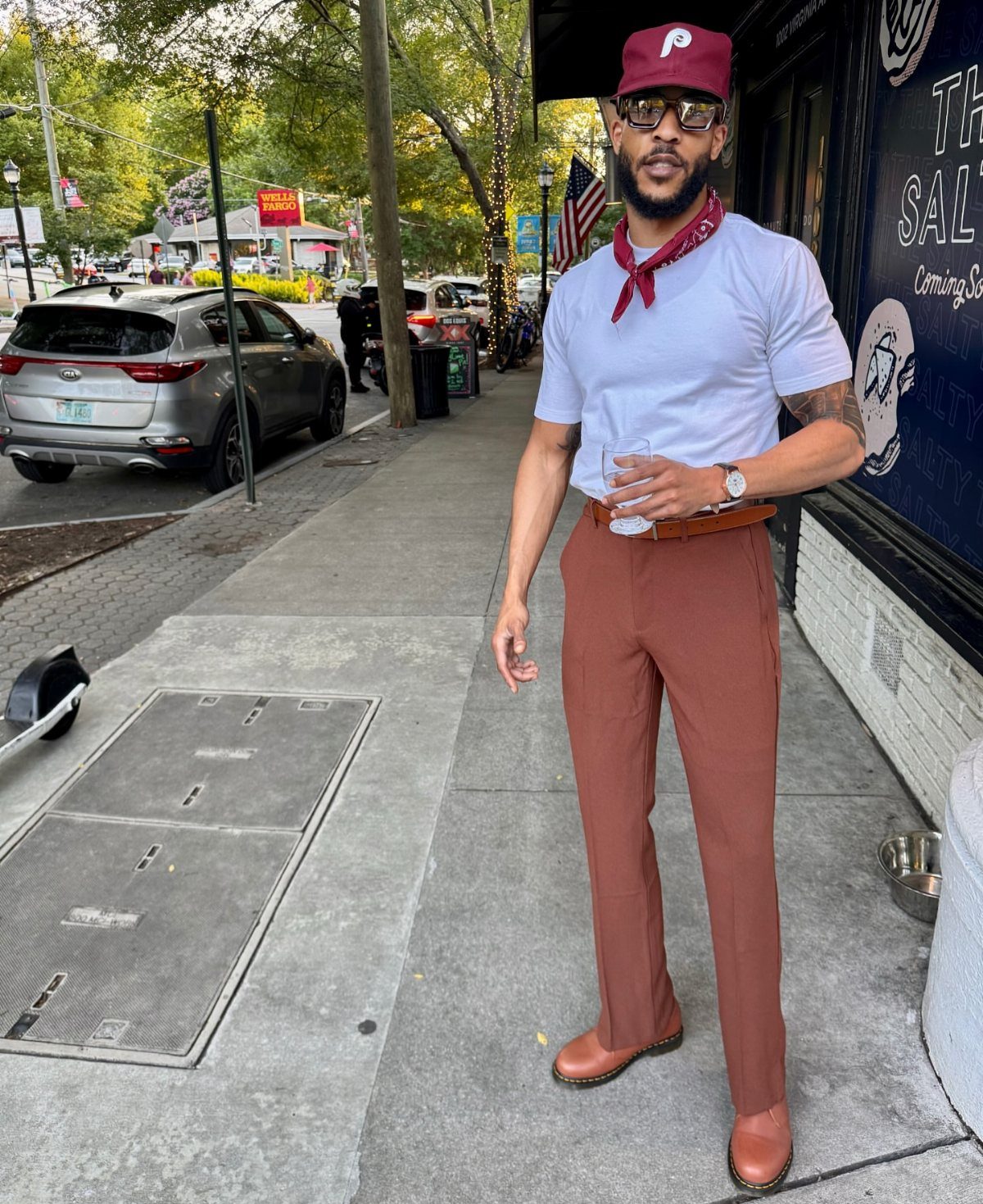 A man posing on a sidewalk wearing a white t-shirt and brown chinos.